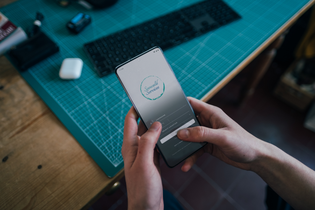 Person hält Smartphone mit Seewald Services Logo über Schreibtisch mit Tastatur, Symbolfoto für digitalen Buchhaltungsservice.